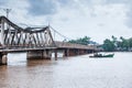 Landscape orientation view, couple fisherman with old fishing boat pass under the old French bridge over the Praek Tuek Chhu River